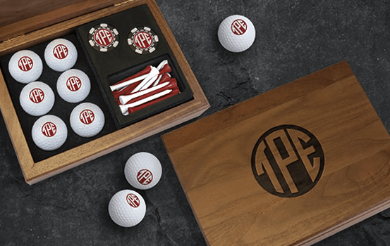 Wooden golf gift set containing personalized golf balls, tees, and accessories beside a monogrammed lid.